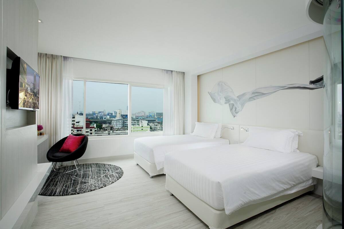 Ein Hotelzimmer mit zwei Betten, Blick auf die Stadt, einem modernen Sessel und einem großen, abstrakten Gemälde an der Wand.