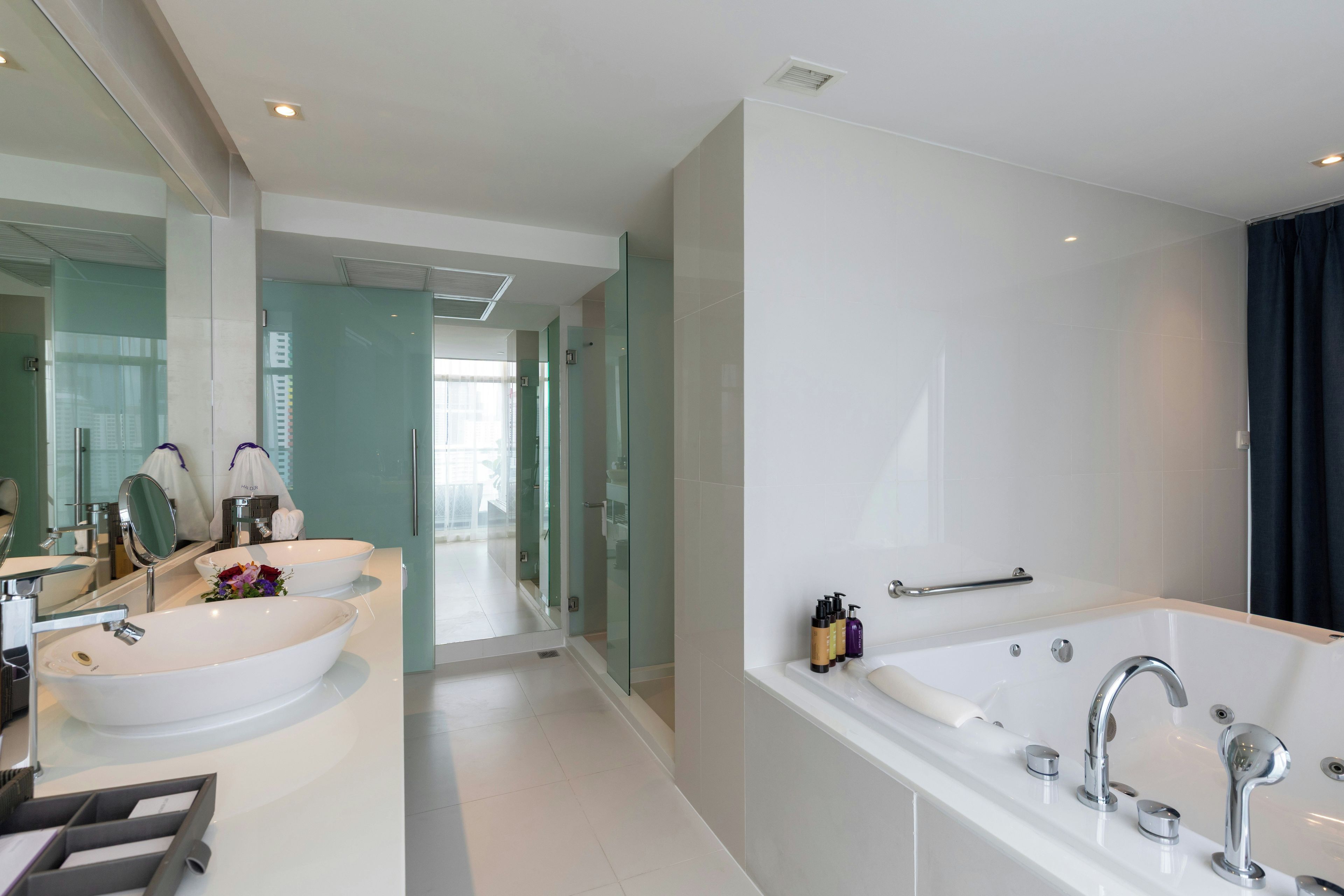 A modern bathroom with a large bathtub, two sinks, and a glass-enclosed shower area.