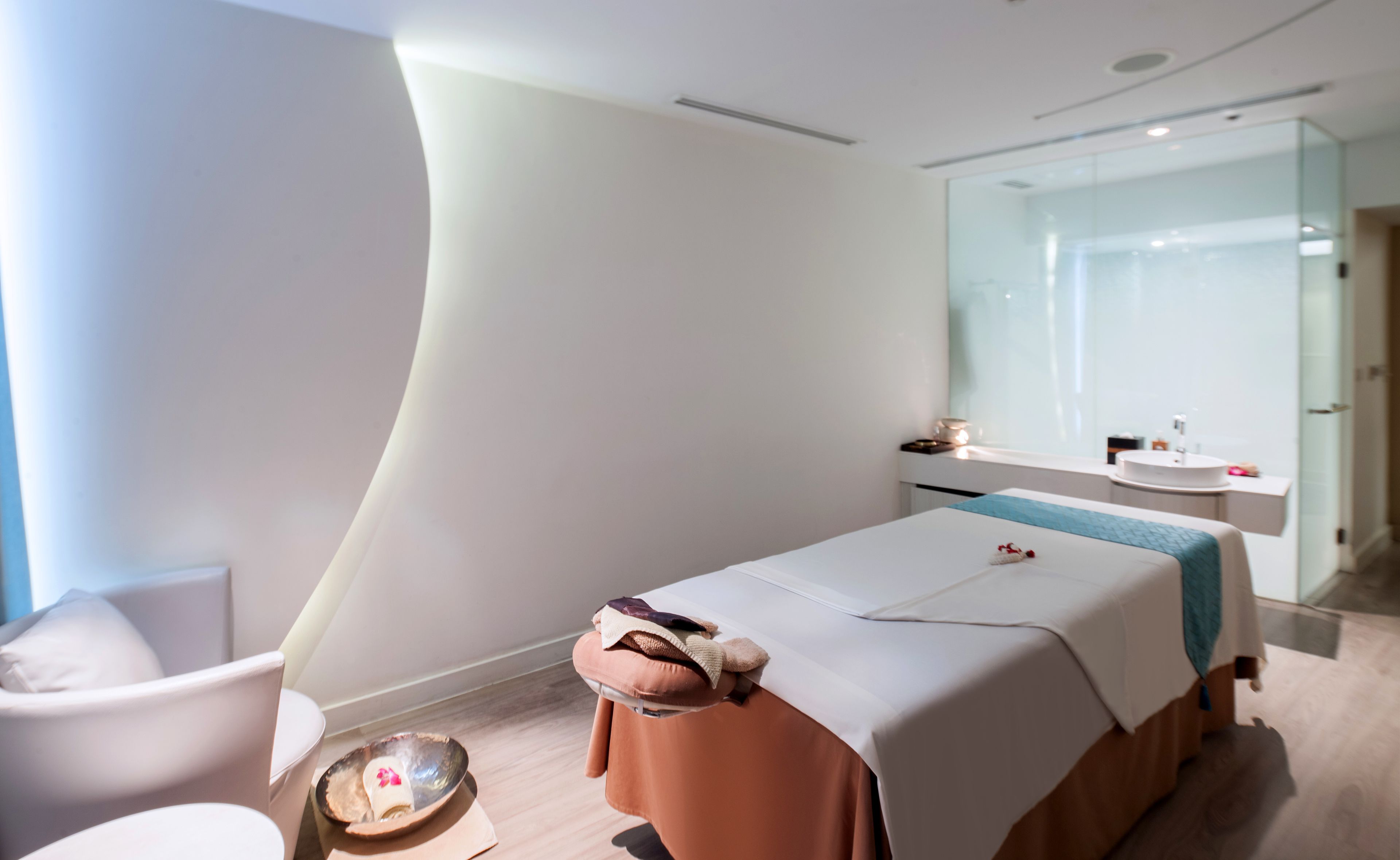Una moderna sala spa con un lettino da massaggio, una poltrona e uno specchio grande.