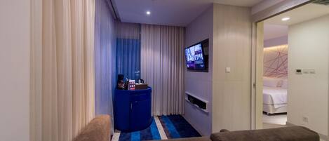A modern hotel room with a large bed, a TV mounted on the wall, a small blue side table with a coffee machine, and a blue and white striped rug.