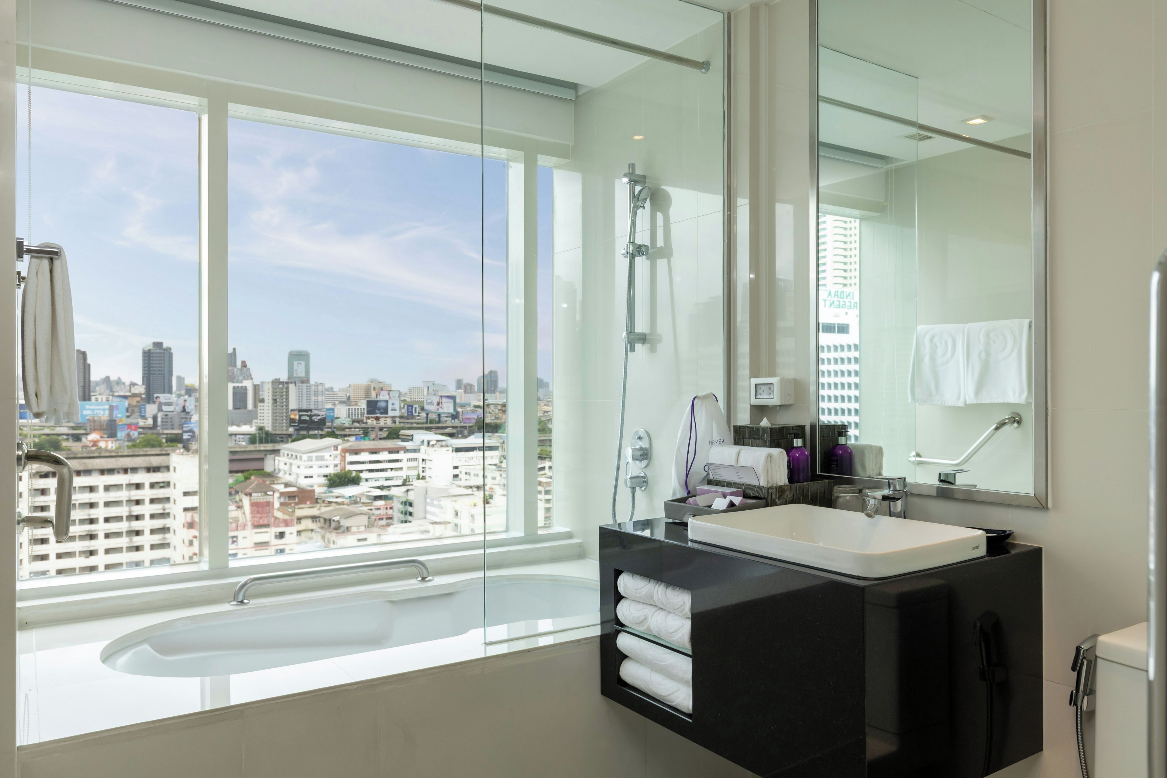 A modern bathroom with a large window, a bathtub, a vanity with a mirror, and a shower.