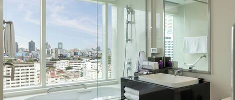 A modern bathroom with a large window, a bathtub, a vanity with a mirror, and a shower.