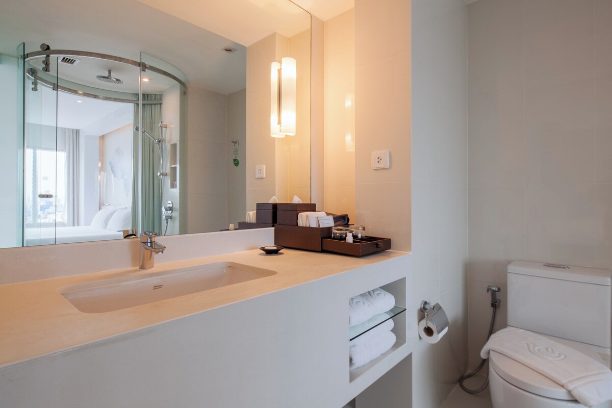 Un baño moderno con un espejo grande, un lavamanos blanco, una ducha y un inodoro.