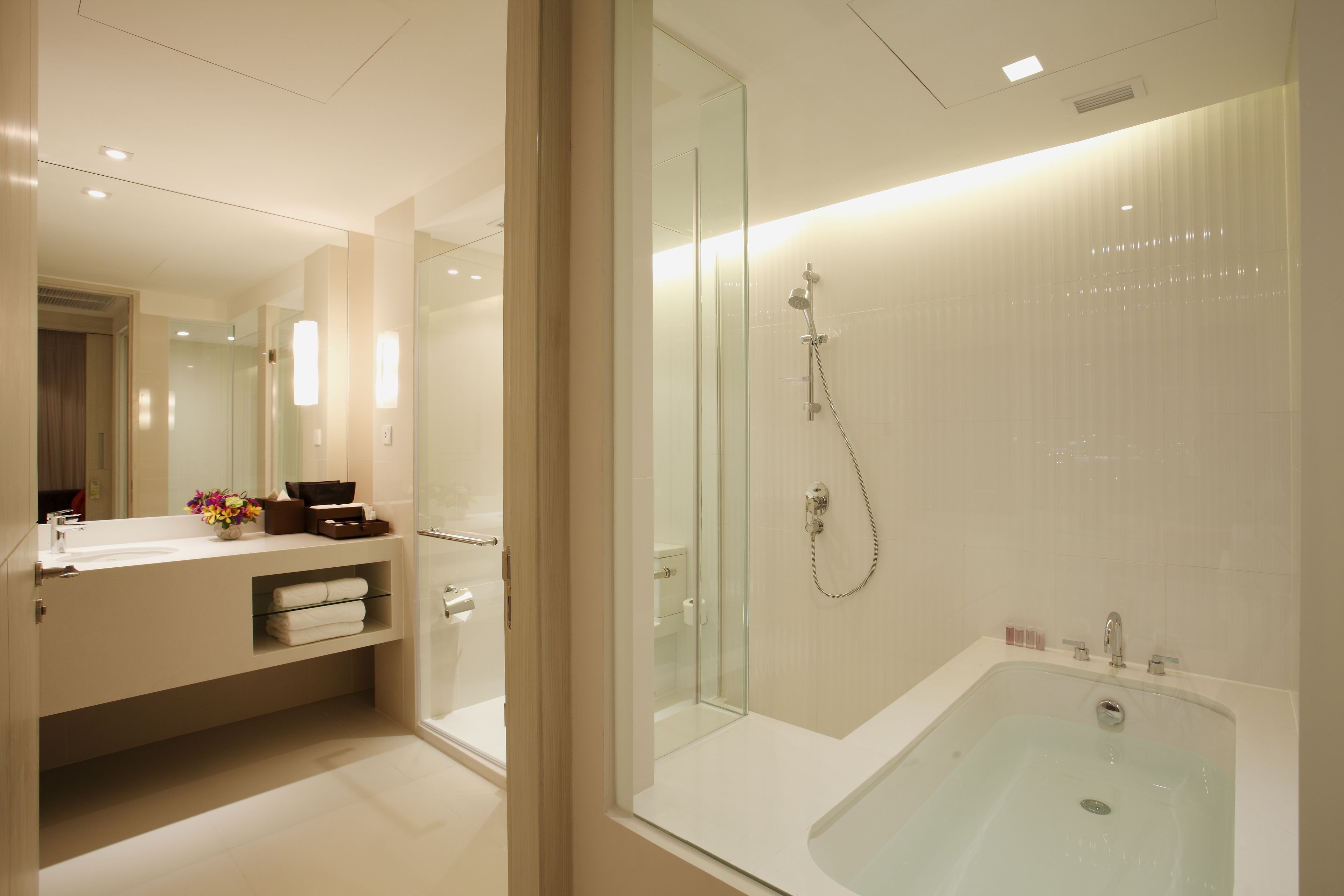 Un baño moderno con ducha envuelta en vidrio, una bañera grande y un tocador con espejo.