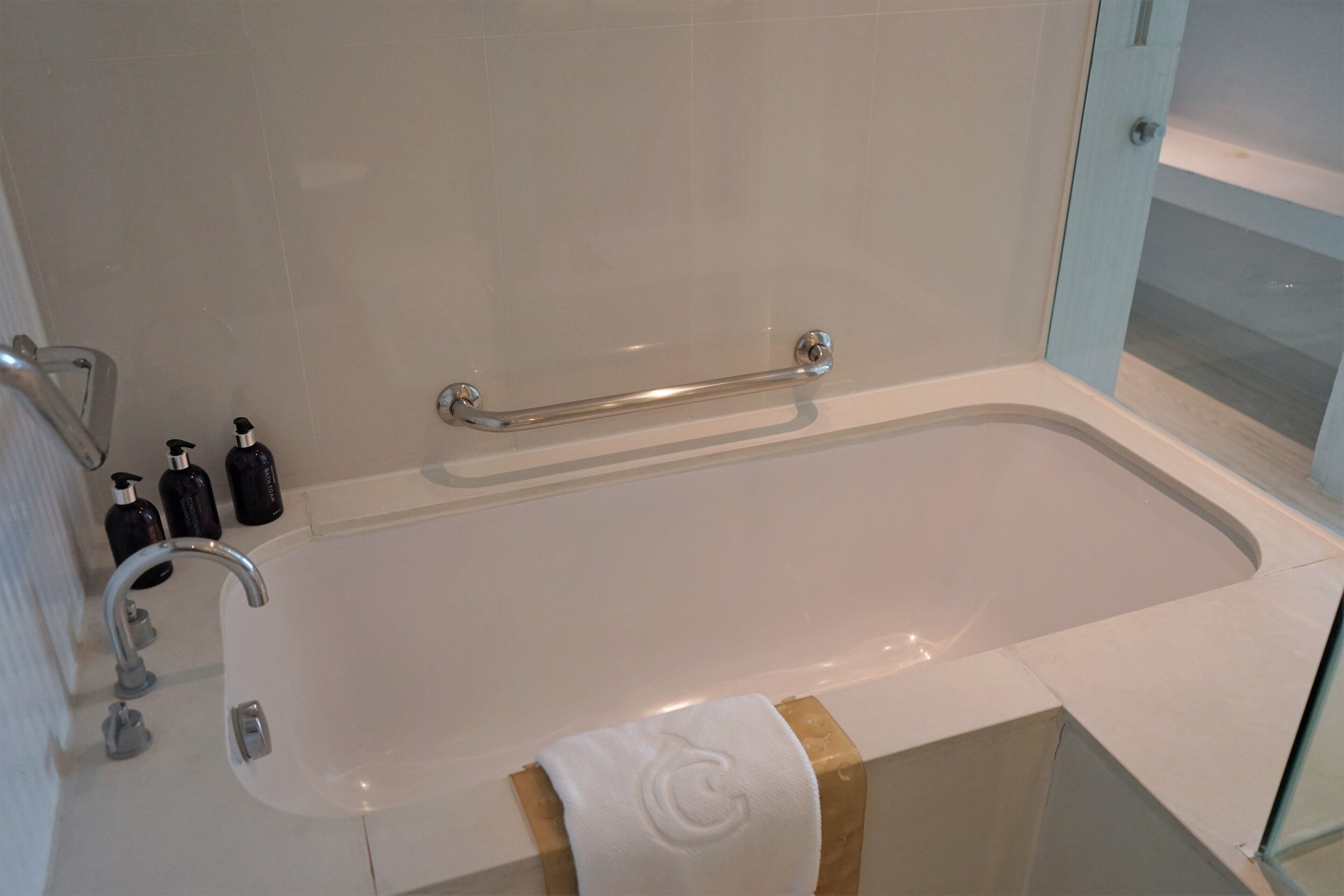 Un baño moderno con bañera, barras de apoyo y un perchero para toallas.