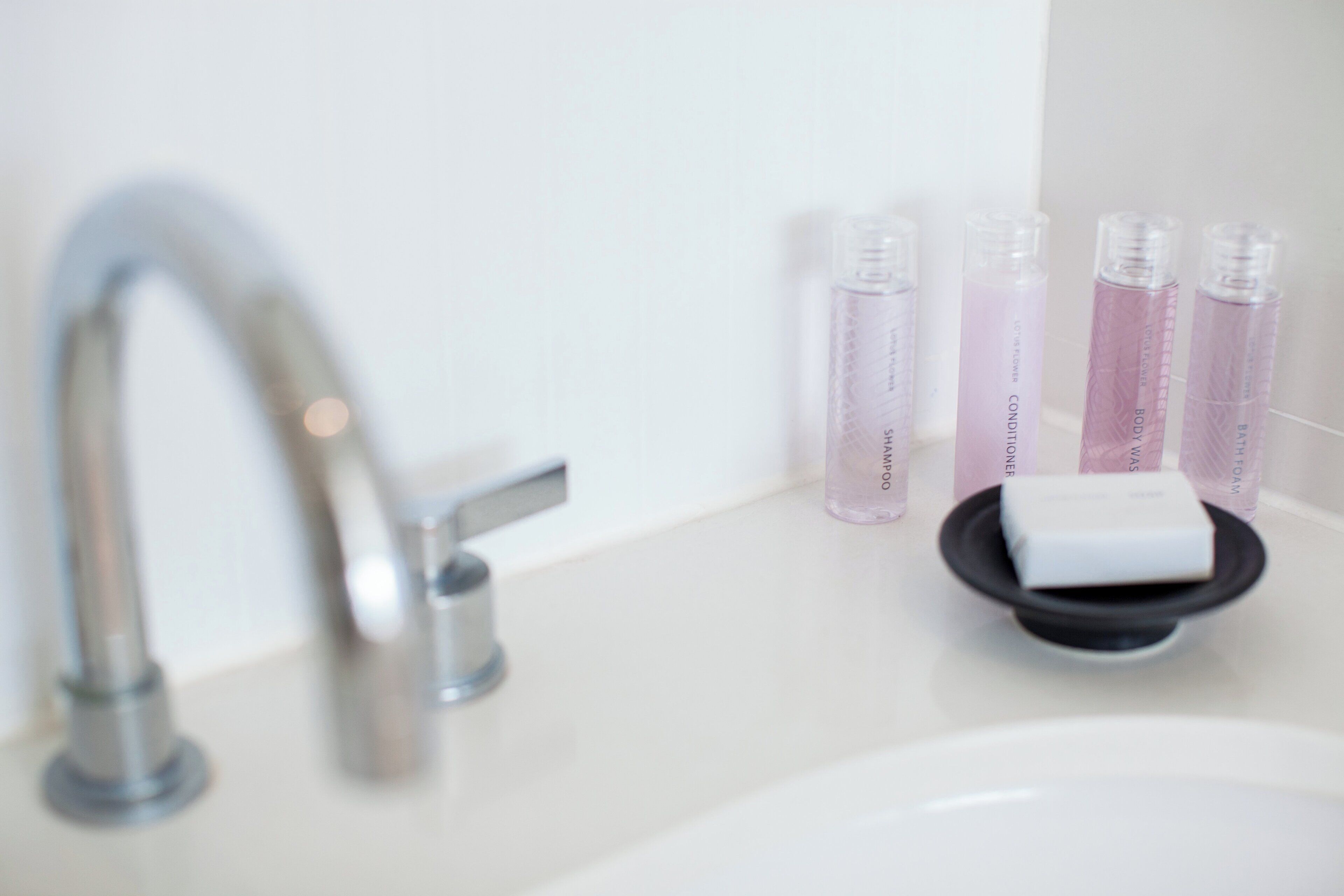 A bathroom sink with a modern faucet, a soap dish, and four bottles of lotion.
