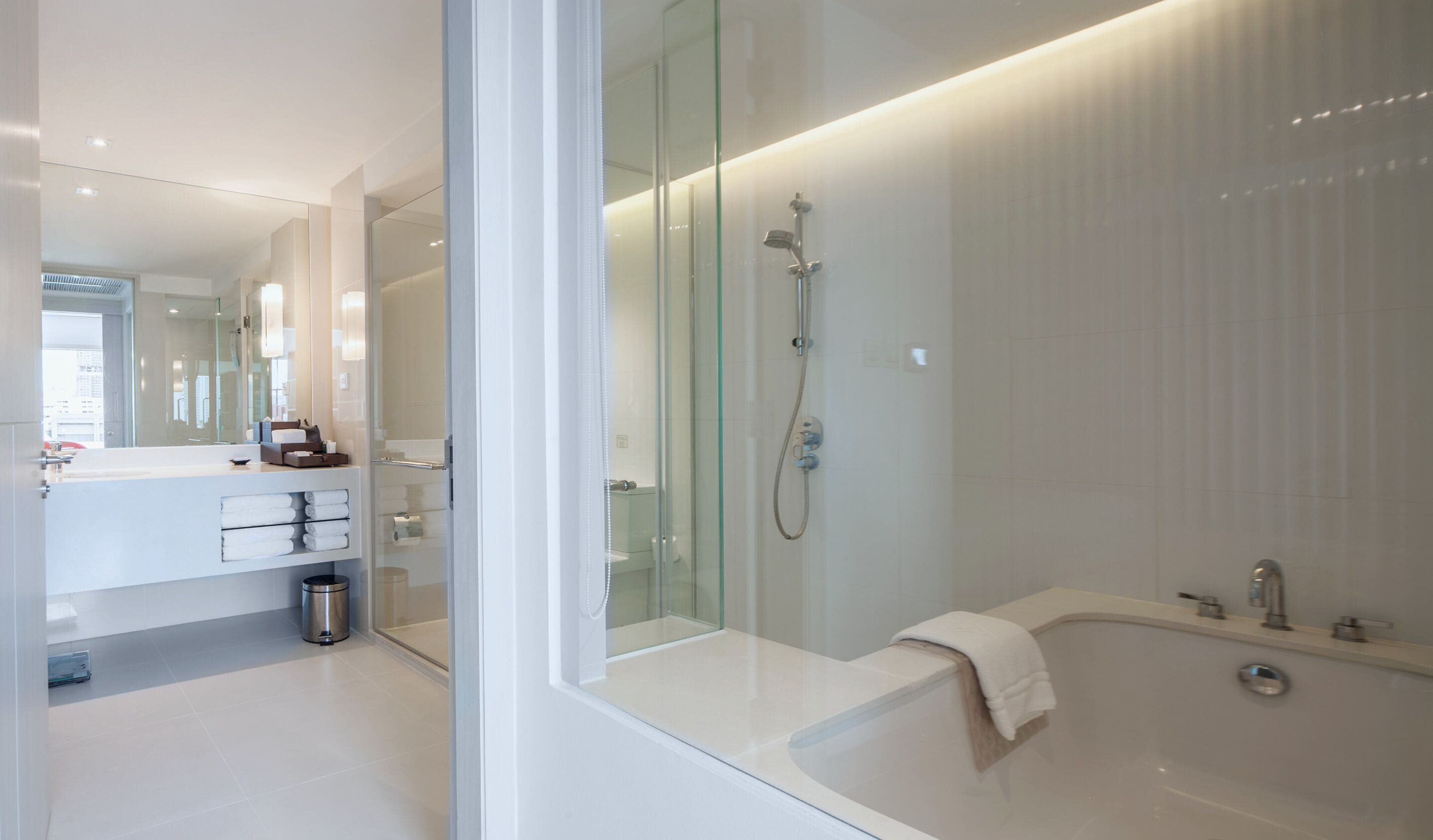 A modern bathroom with a glass shower enclosure, a white bathtub, and a vanity with a mirror and towel rack.