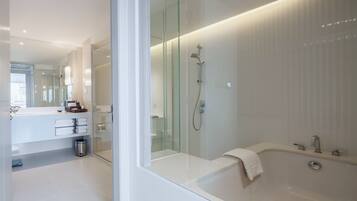 A modern bathroom with a glass shower enclosure, a white bathtub, and a vanity with a mirror and towel rack.