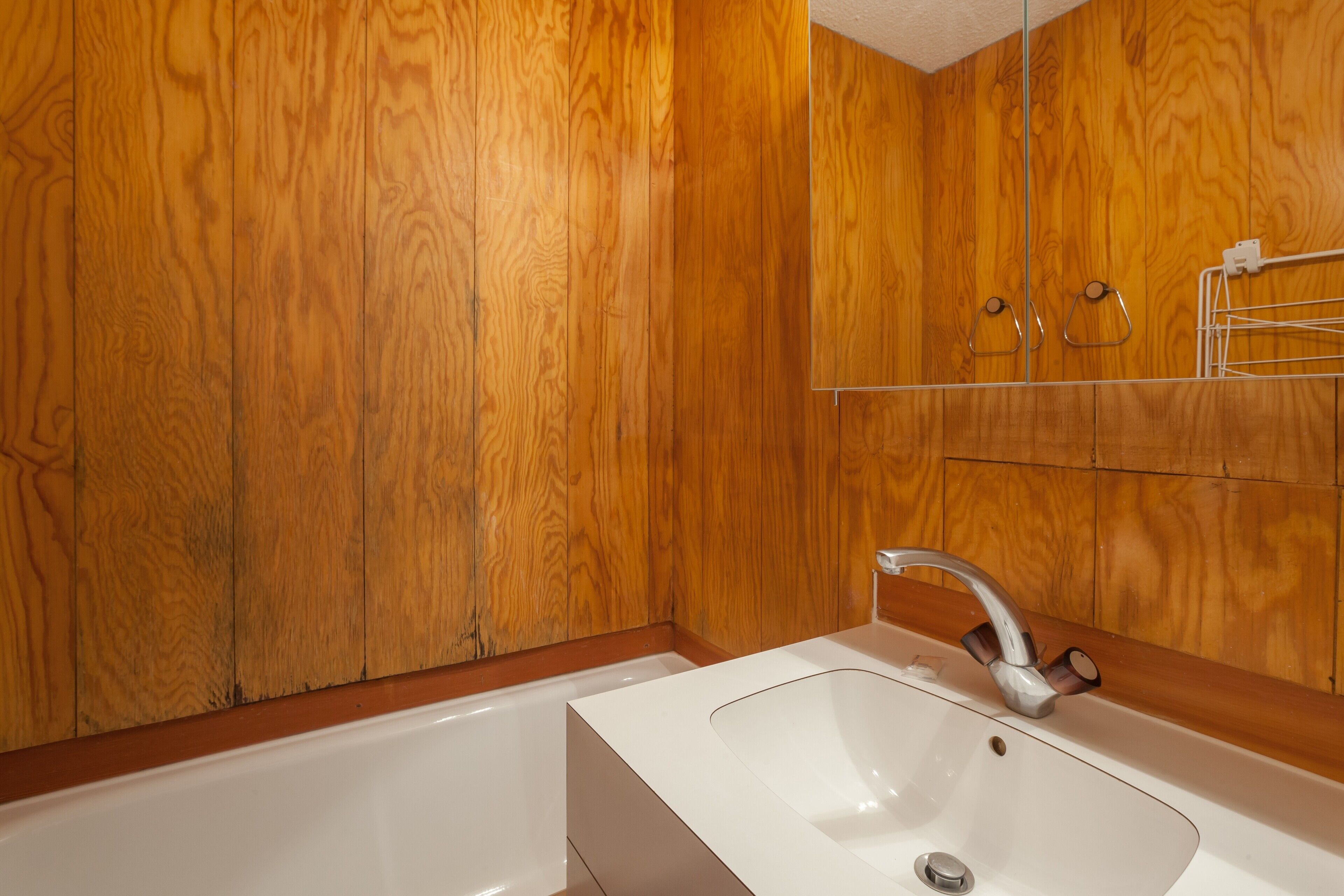 A bathroom with wooden panel walls, a white sink, and a mirror.