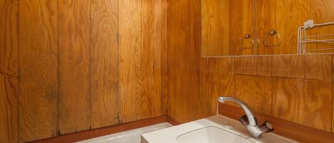 A bathroom with wooden panel walls, a white sink, and a mirror.