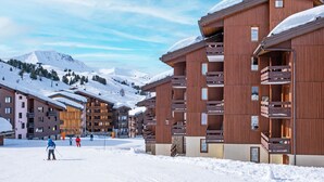 Ein Skigebiet mit mehrstöckigen Holzhäusern, Skipisten und schneebedeckten Bergen im Hintergrund.