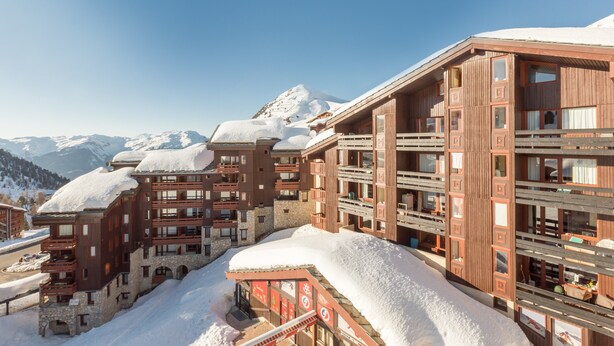 Ein mehrstöckiges Hotel mit Balkonen und einem mit Schnee bedeckten Dach, vor einer Bergkulisse gelegen.