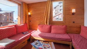 Ein gemütliches Zimmer mit Holzwänden, einer Couch mit roten Kissen, einem Holztisch mit Zeitschriften und einem Fenster mit Vorhängen.