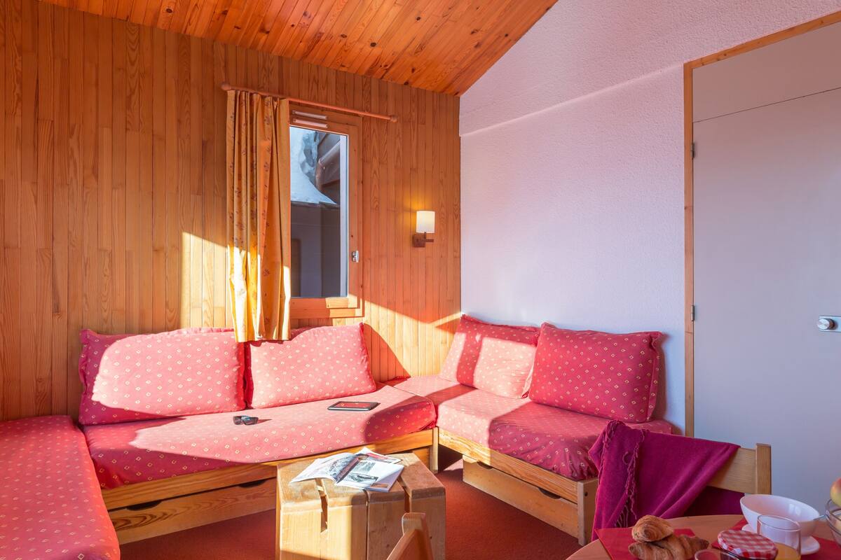Un chalet en bois accueillant, avec un canapé-lit, une table en bois sur laquelle sont disposés des articles pour le petit-déjeuner, et une fenêtre avec des rideaux.