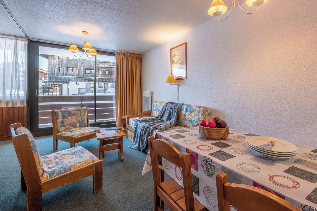 A dining area with a table set for two, a sofa, and a window with a view of buildings.