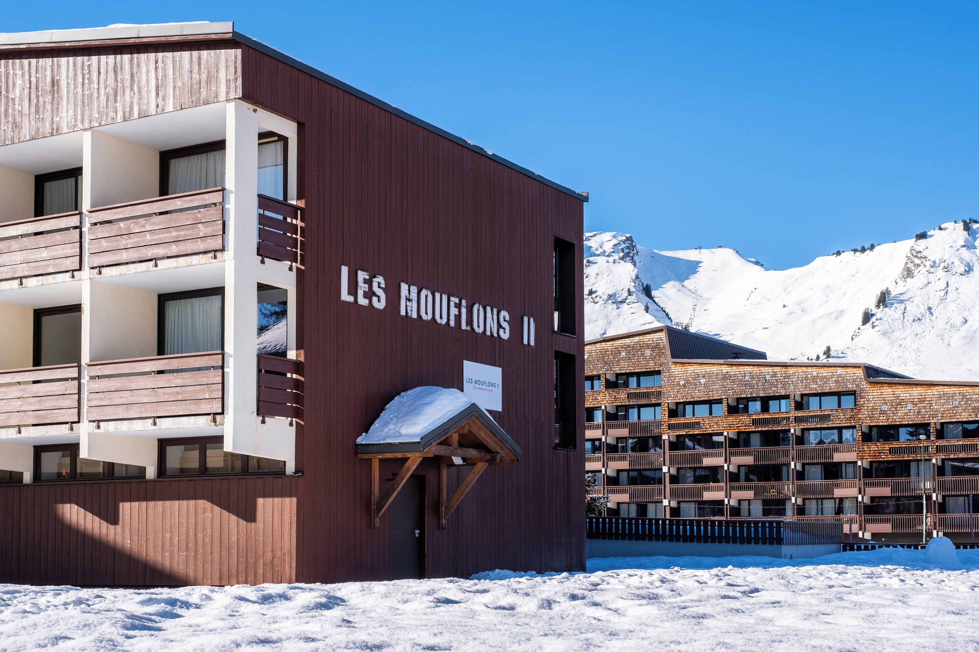 Un edificio con un letrero que dice "LES MOUFLONS II" y un balcón cubierto de nieve.