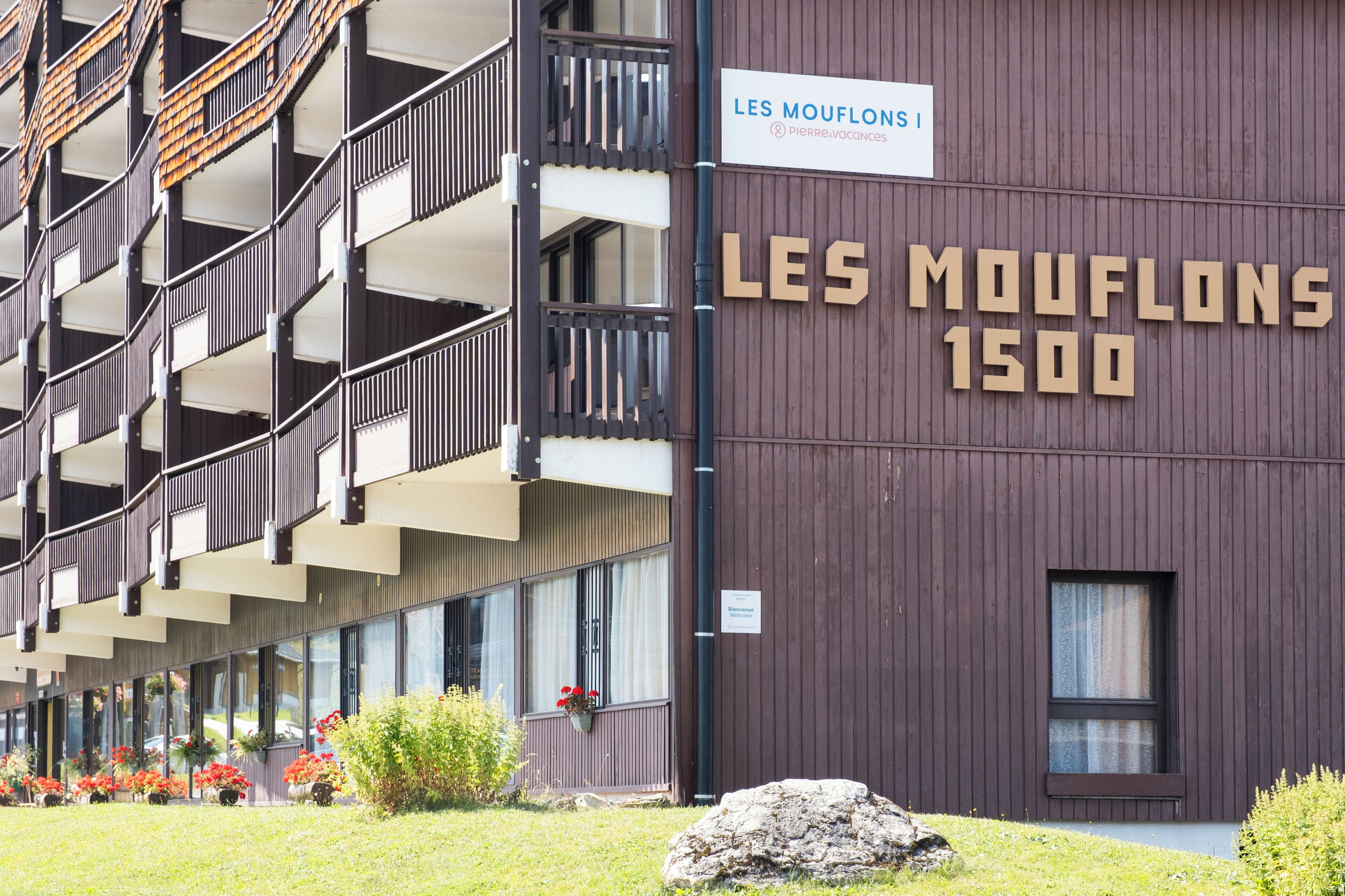 Un edificio con un letrero que dice 'LES MOUFLONS 1500', balcones y una ventana con cortina.