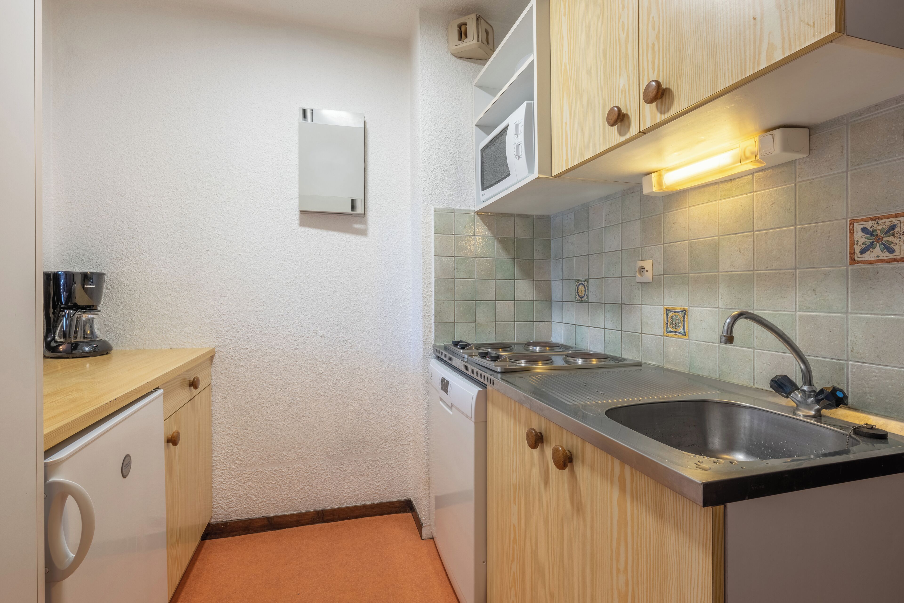 A compact kitchen with a microwave, stove, sink, and a coffee maker on a wooden countertop.