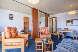Habitación de hotel con cama, dos sillas, una mesita, escritorio, estantería y puerta corredera.