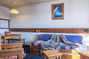 Una habitación acogedora con un banco de madera, una mesa con manzanas, un sofá con una manta y un reloj en la pared.