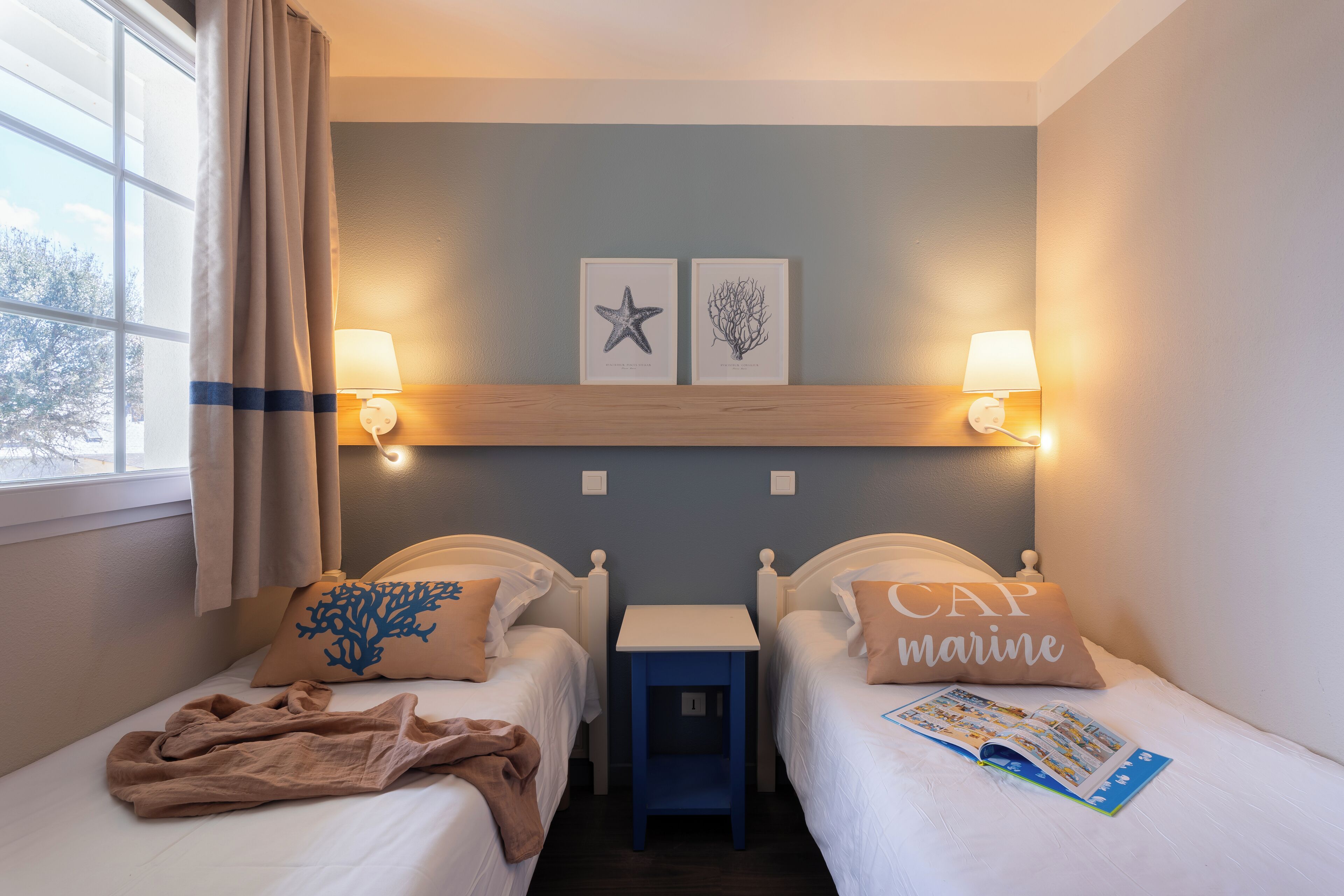 Een hotelkamer met twee bedden, een nachtkastje, een lamp en twee foto's aan de muur.