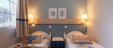 A hotel room with two beds, a nightstand, a lamp, and two wall-mounted pictures.
