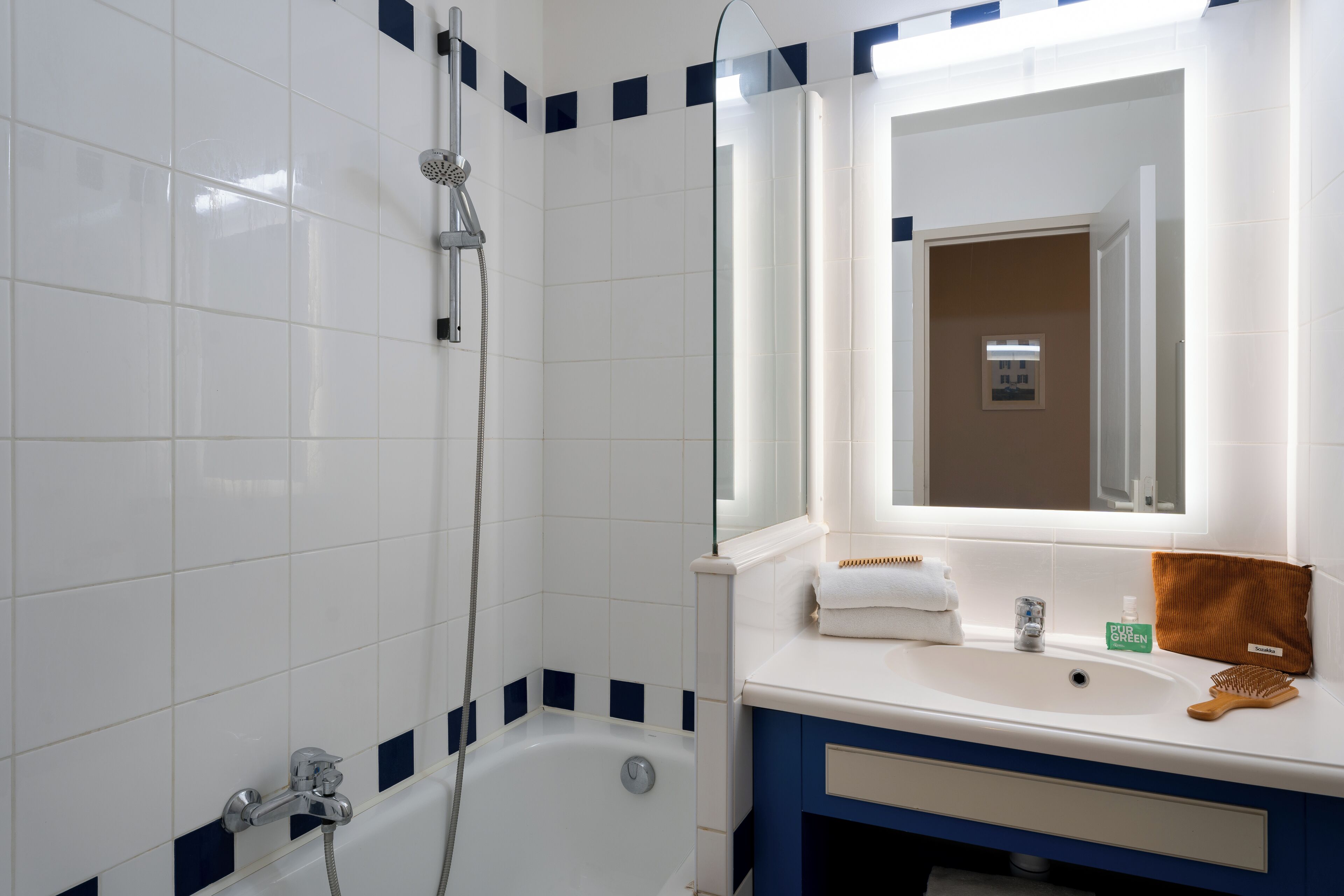 A bathroom with white tiles, a bathtub, a shower, a sink with a mirror, and a towel rack.