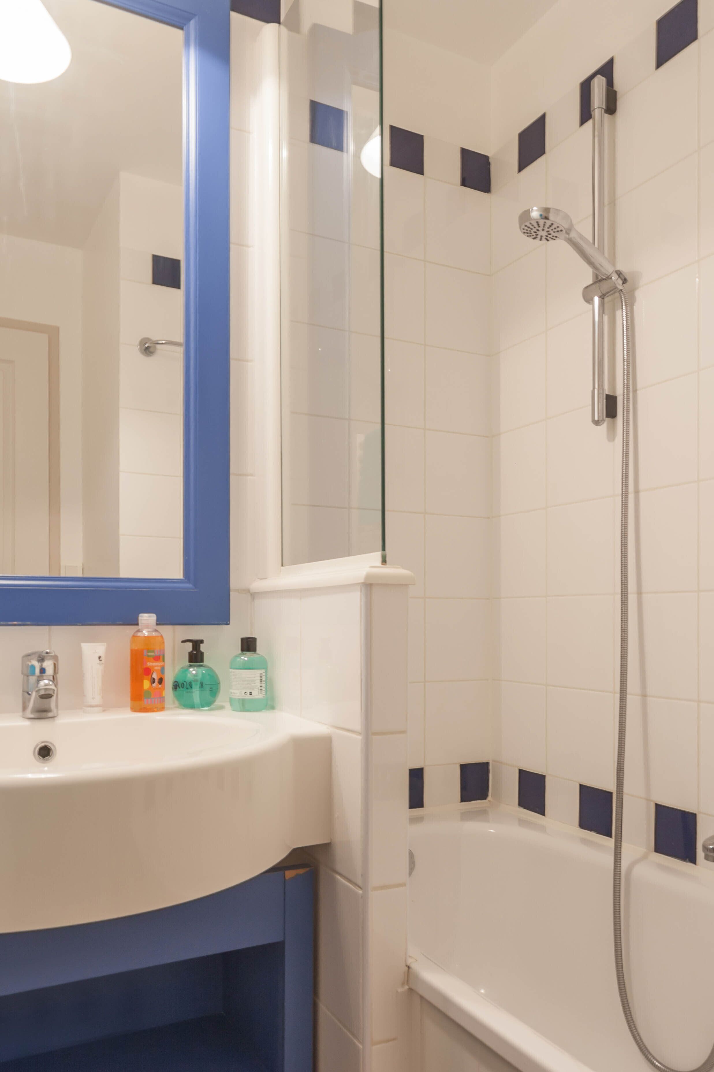 Ein Badezimmer mit einem weißen Waschbecken, einem blauen Schrank und einer Duschkabine aus Glas.