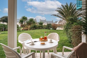 A round table with chairs, a tray with food and drinks, and a view of a building in the background. - Résidence Pierre & Vacances Cap Marine (Guilvinec)