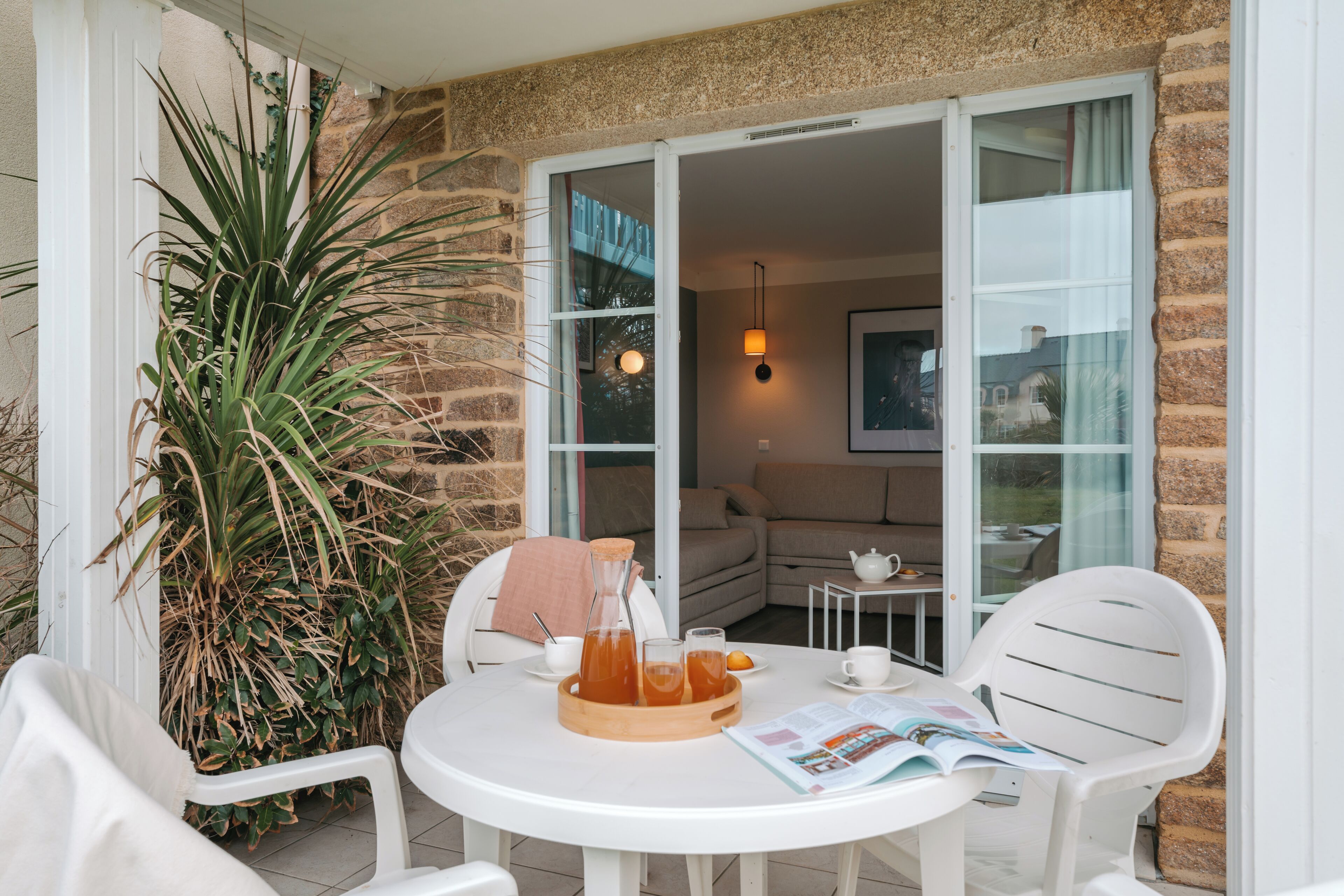 A patio with a round table, chairs, a potted plant, and a beverage setup.