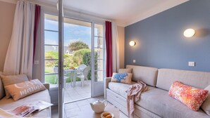 A modern living room with a sofa, a coffee table, and a view of the garden through a glass door. - Résidence Pierre & Vacances Cap Marine (Guilvinec)