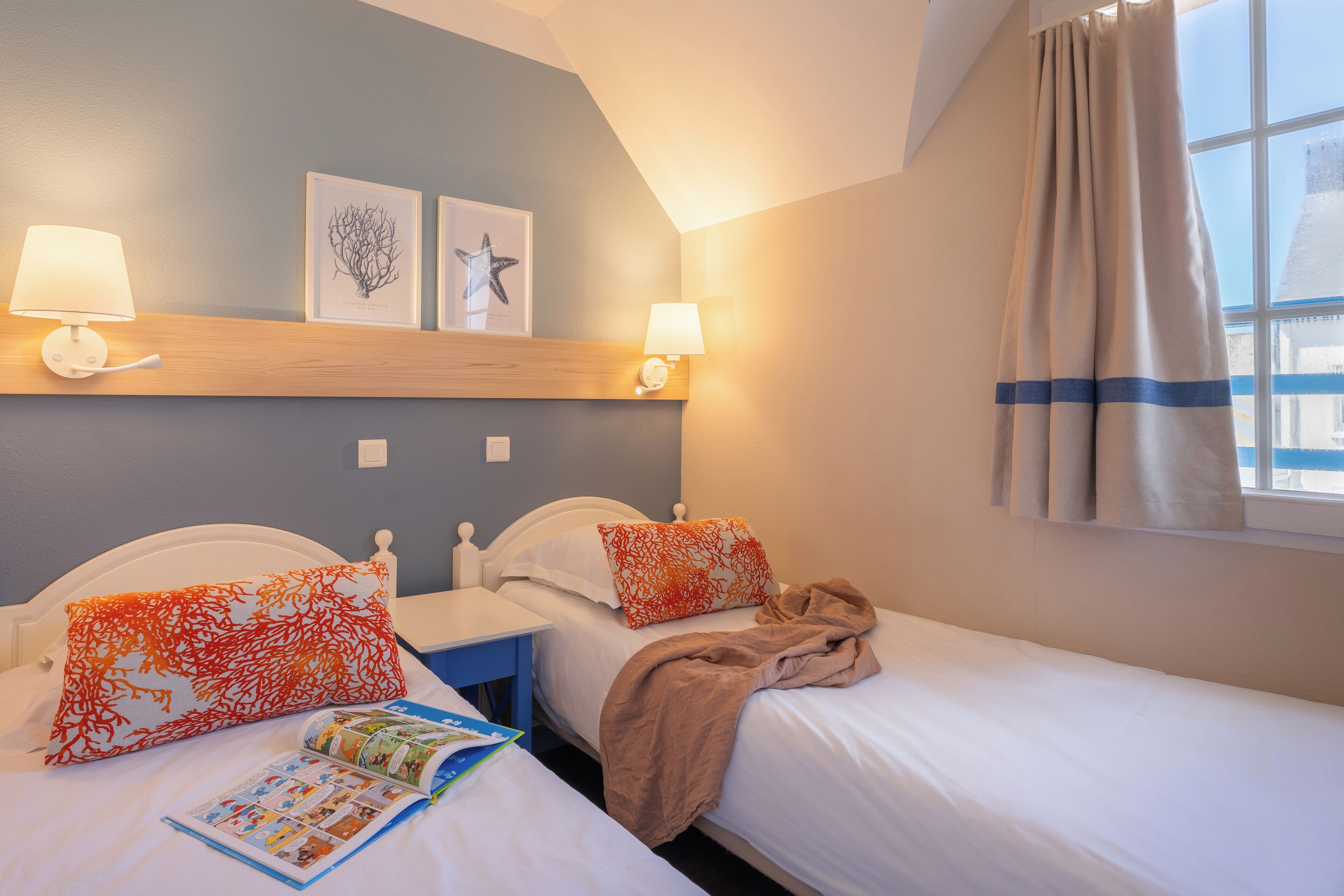 Une chambre d’hôtel avec deux lits, une table de chevet, une fenêtre avec des rideaux et des lampes fixées au mur.