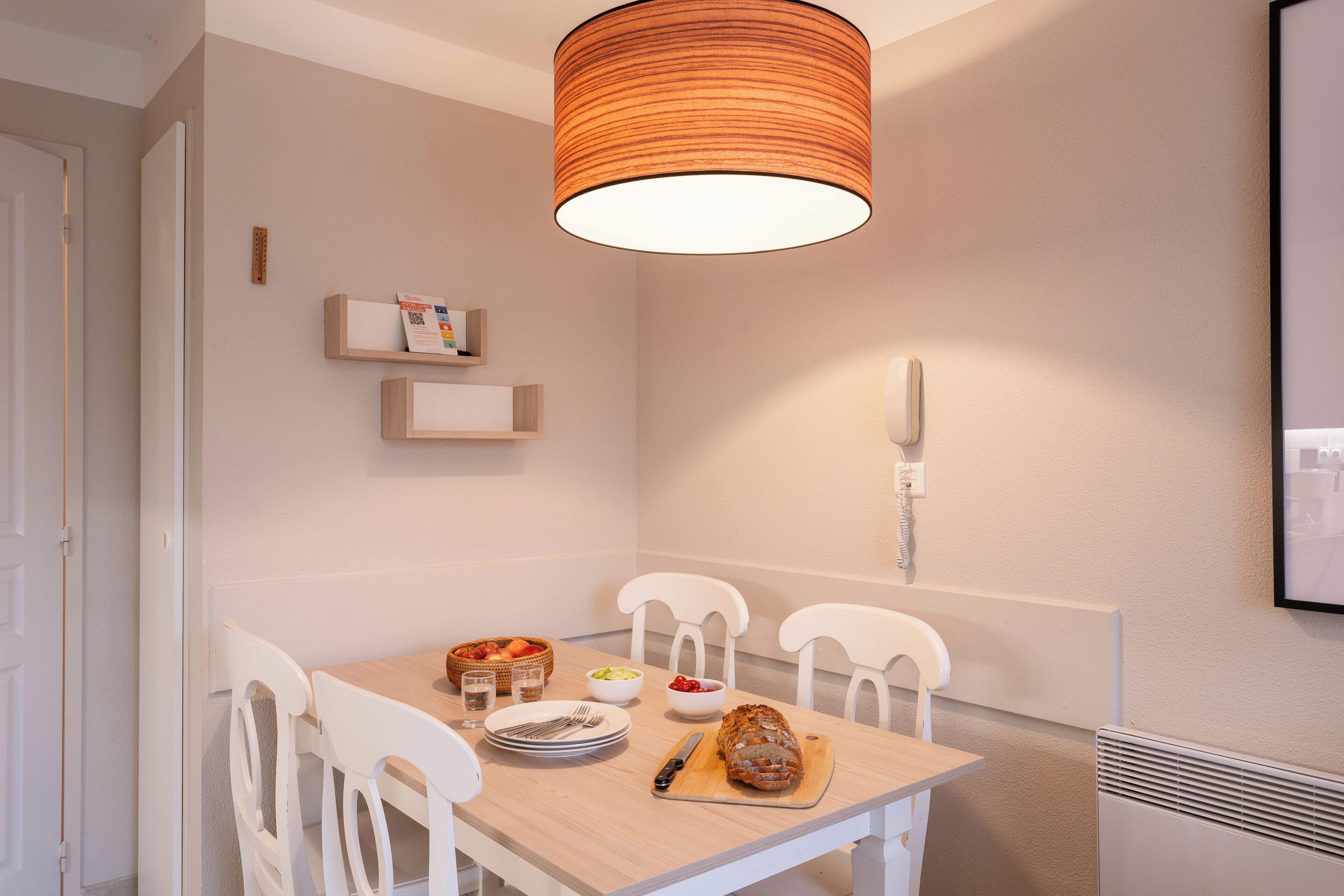 Un comedor con mesa de madera, sillas blancas, una hogaza de pan y un frutero.