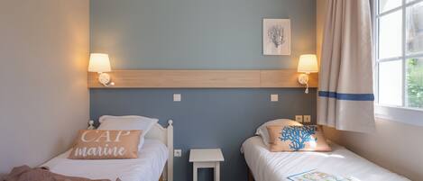 A bedroom with two beds, a nightstand, a small table, and a window with curtains.