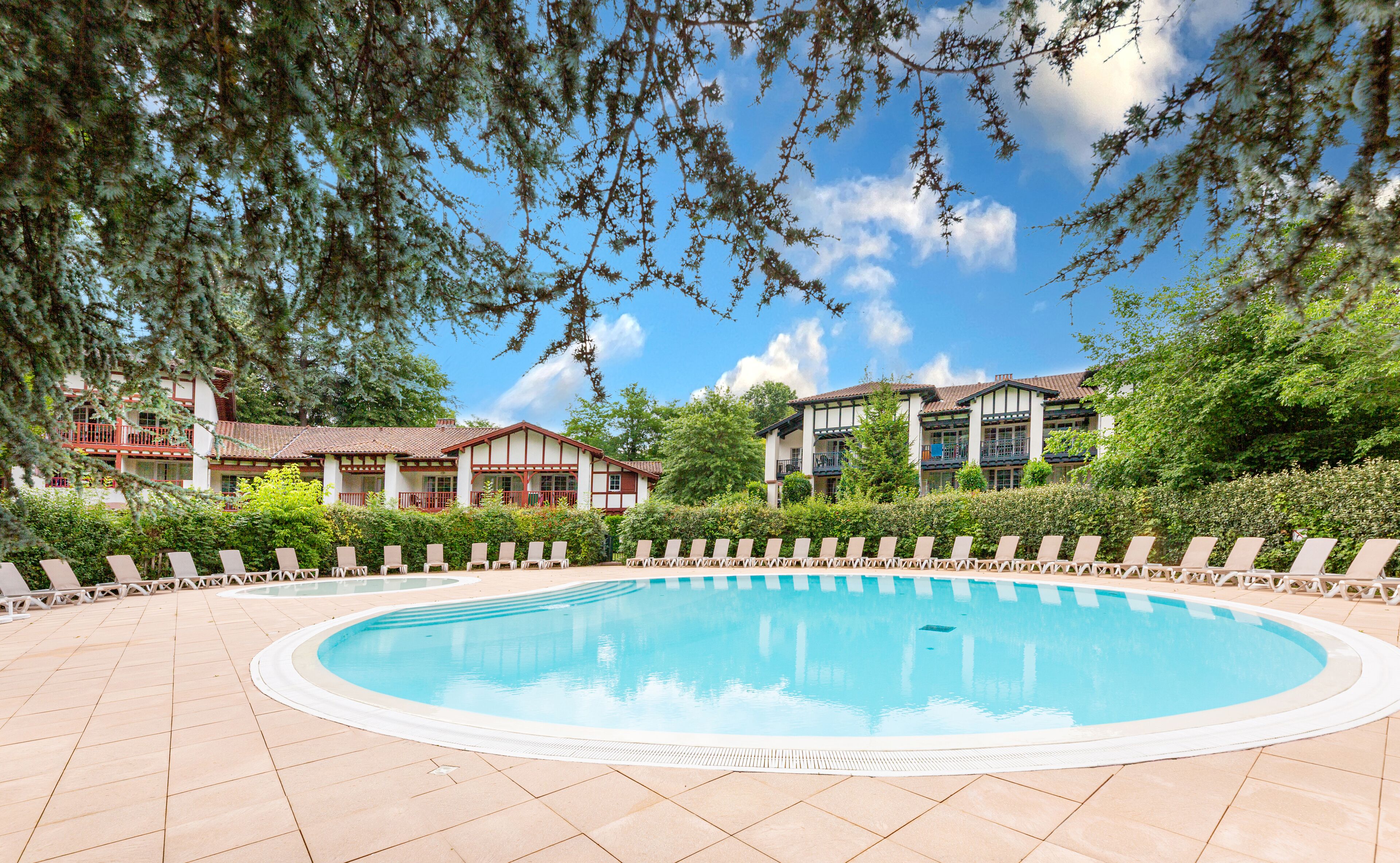 A pool area with lounge chairs and a building with a tiled roof.