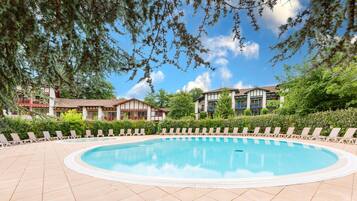 A pool area with lounge chairs and a building with a tiled roof.