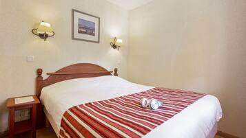 A hotel room with a wooden bed, a striped blanket, two wall-mounted lamps, and a framed picture on the wall.