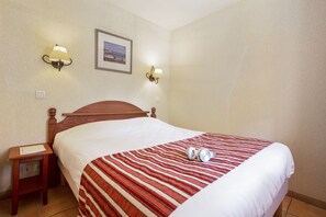 Habitación de hotel con una cama de madera, un edredón a rayas, dos lámparas fijadas a la pared y un cuadro enmarcado.
