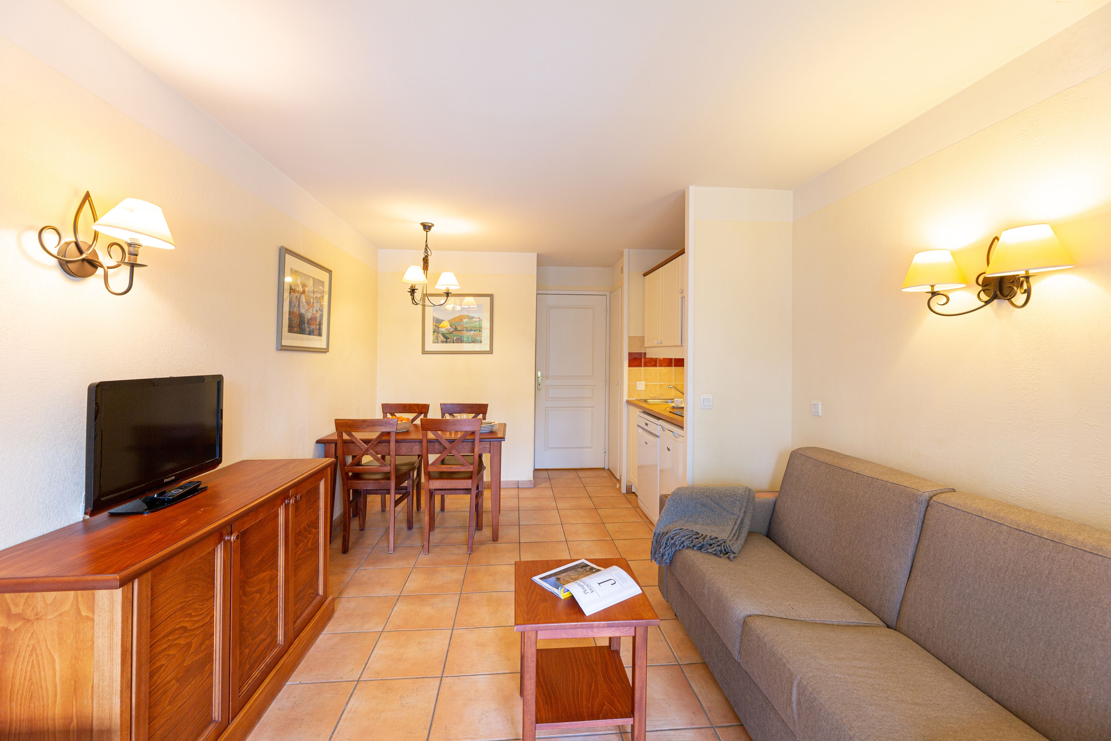 A living room with a TV, wooden furniture, a sofa, and wall-mounted lights.