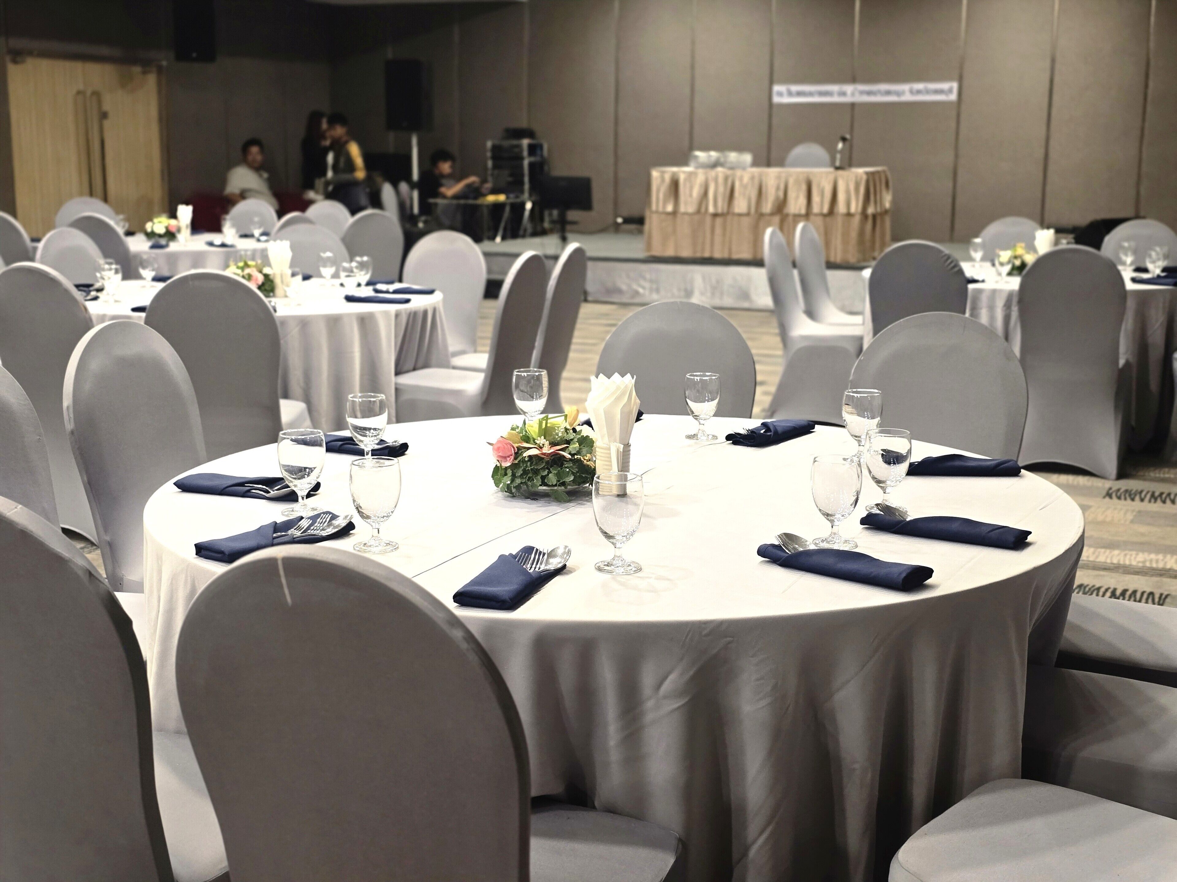 A conference room with round tables, grey chairs, and a stage in the background.