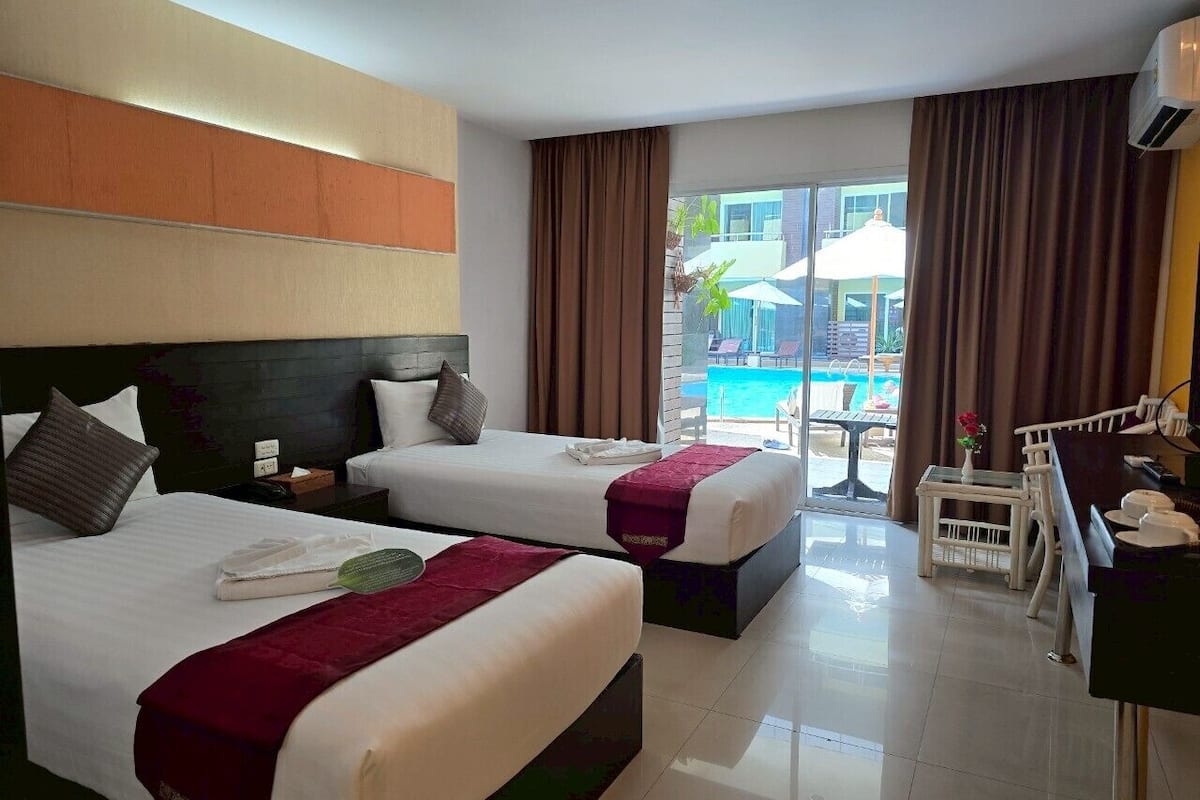 A hotel room with two beds, a desk, and a view of an outdoor swimming pool.