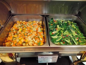 Buffet com dois acompanhamentos: um com legumes e arroz picados, outro com folhas verdes e vegetais.