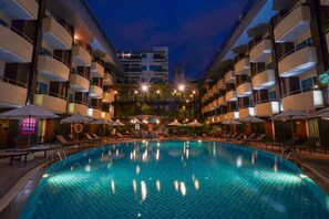 A swimming pool with lounge chairs and umbrellas, surrounded by multi-story buildings with balconies. - Baron Beach Hotel (Pattaya)