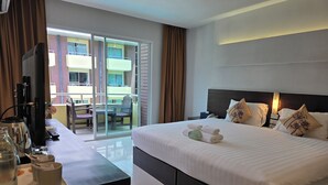 A hotel room with a bed, bedside table, TV, and a balcony with a table and chairs. - Baron Beach Hotel (Pattaya)