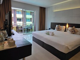Quarto de hotel com cama, mesa de cabeceira, televisão e uma varanda com mesa e cadeiras.