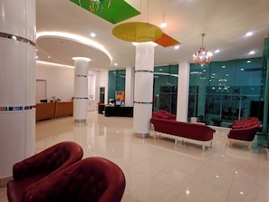 Um lobby moderno com balcão de recepção, assentos vermelhos e uma parede de vidro.