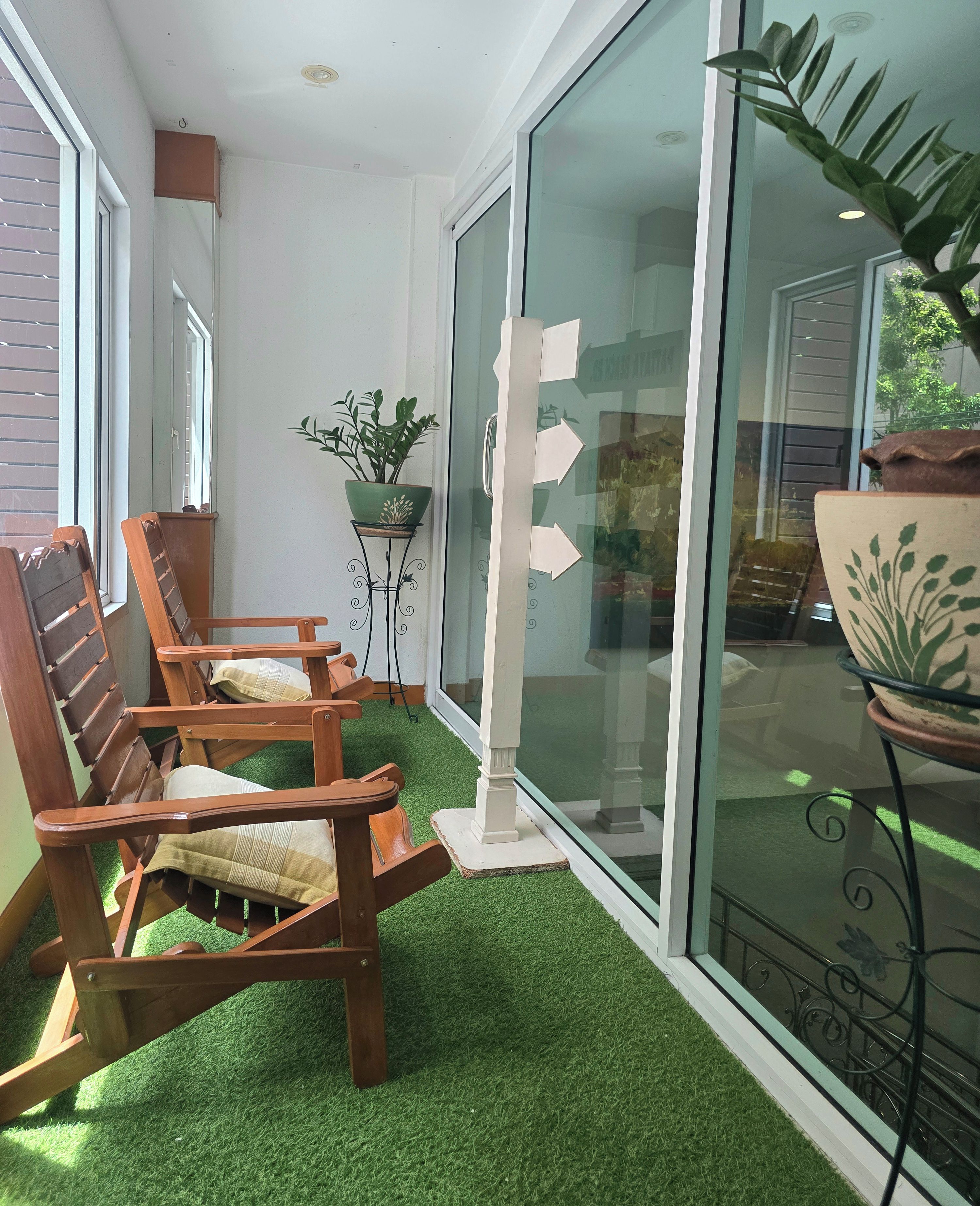 A seating area with wooden chairs and a green artificial turf floor, a potted plant, and a glass door with directional arrows.