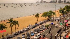 A beachside view with a parking lot, beach, and city skyline. - Baron Beach Hotel (Pattaya)