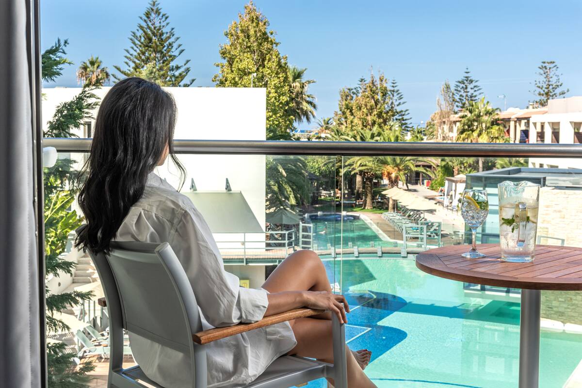 A person seated by a poolside table with a clear view of a pool and surrounding greenery.