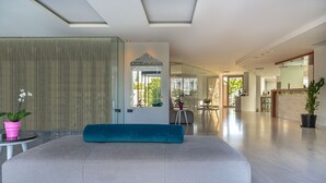A modern living room with a large sofa, a glass partition, and a dining area visible through the partition.